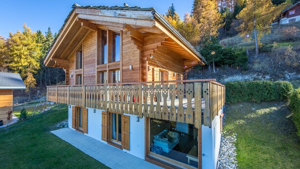 A wooden chalet with a balcony, large windows, and a view of the surrounding forest. - Chalet Asphodel (Haute-Nendaz)