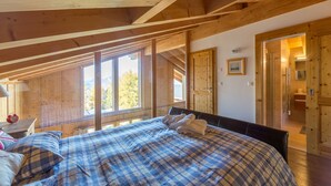 A bedroom with a large bed, wooden beams, a window, and a door leading to a bathroom. - Chalet Asphodel (Haute-Nendaz)