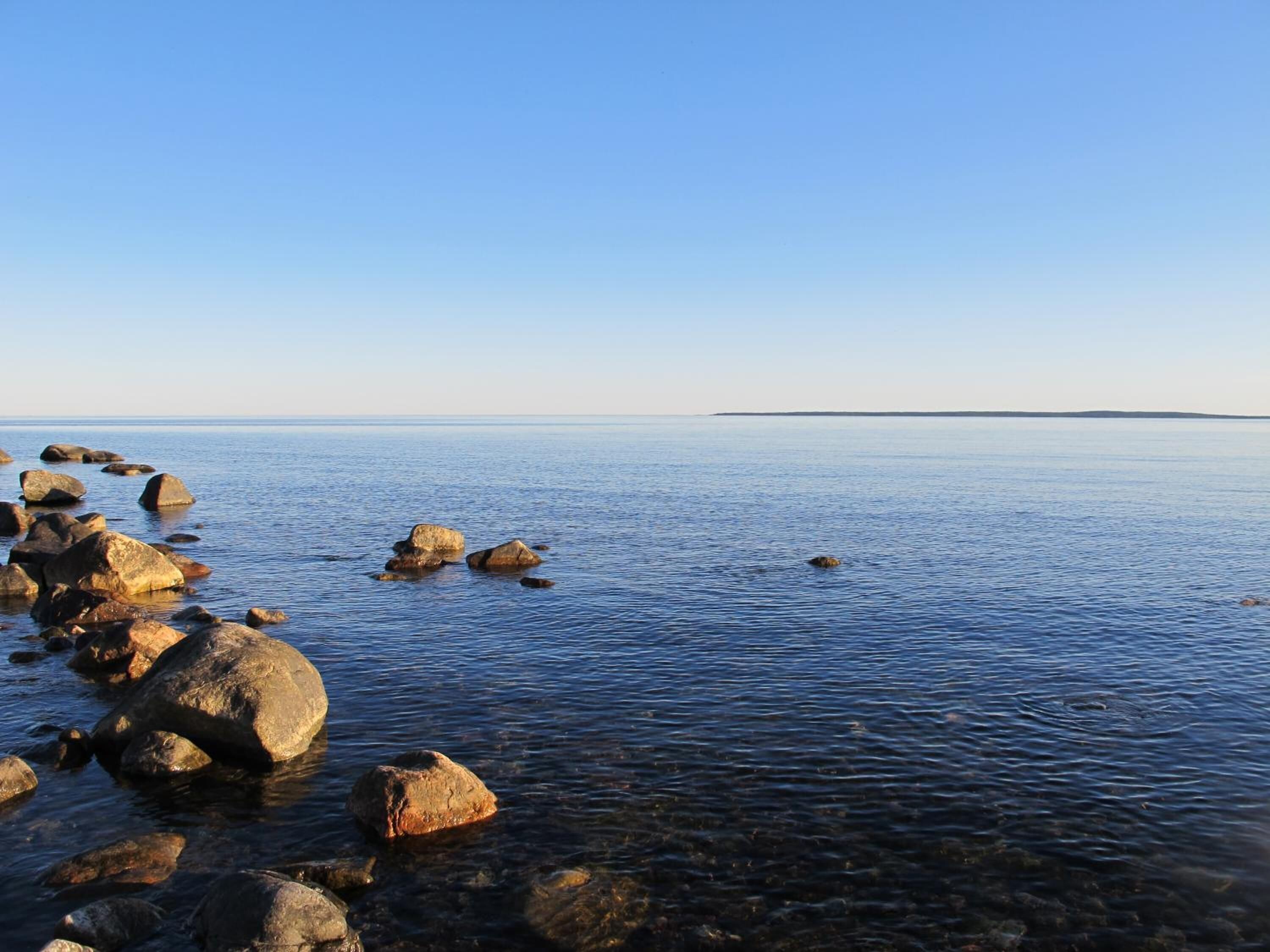 A calm sea with large rocks in the foreground and a clear sky.