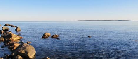 A calm sea with large rocks in the foreground and a clear sky.