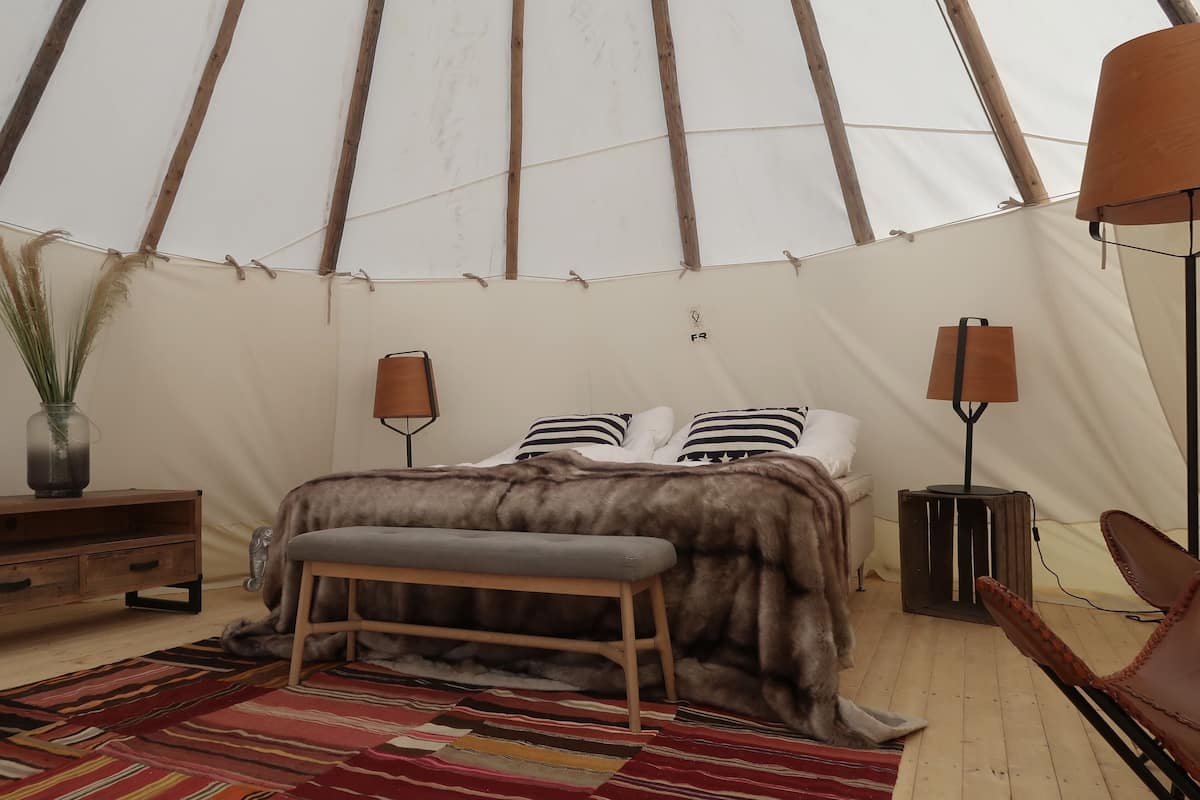 Ein Zelt mit Bett, Bank, Lampe und einem kleinen Tisch.