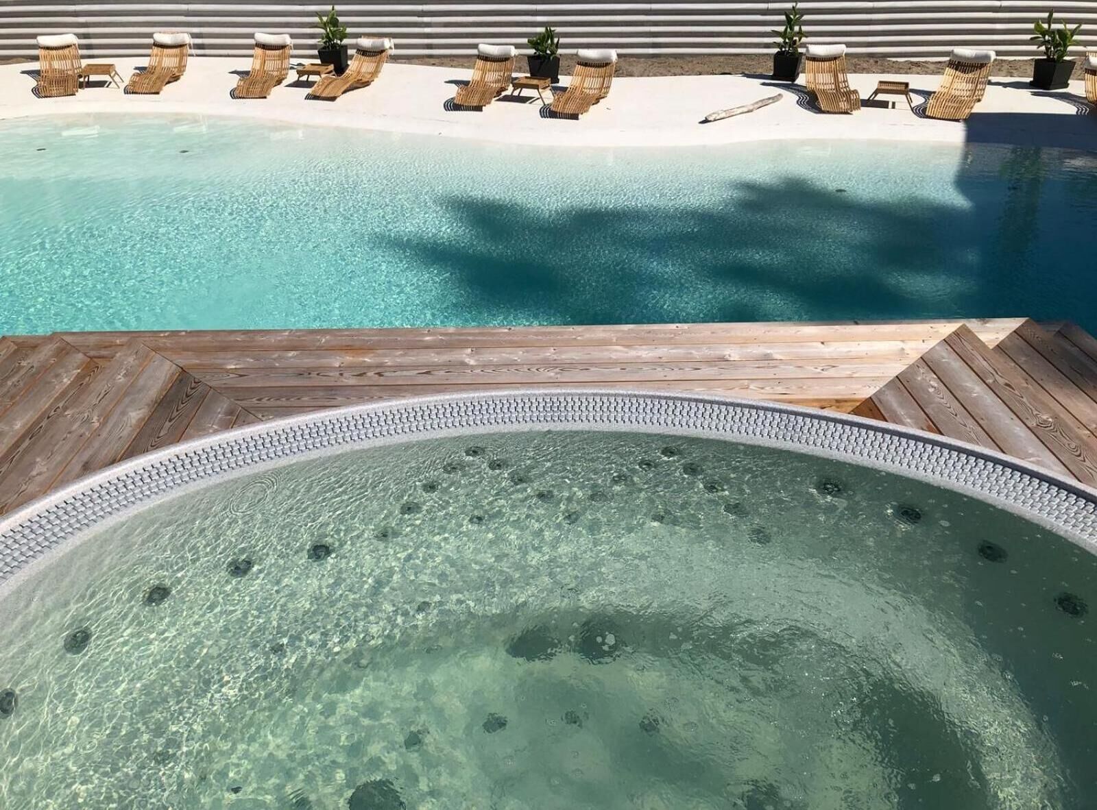 A clear swimming pool with lounge chairs and a hot tub area.