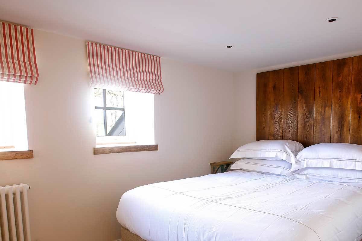 A bedroom with a large bed, two windows with striped valances, a wooden headboard, and a radiator.