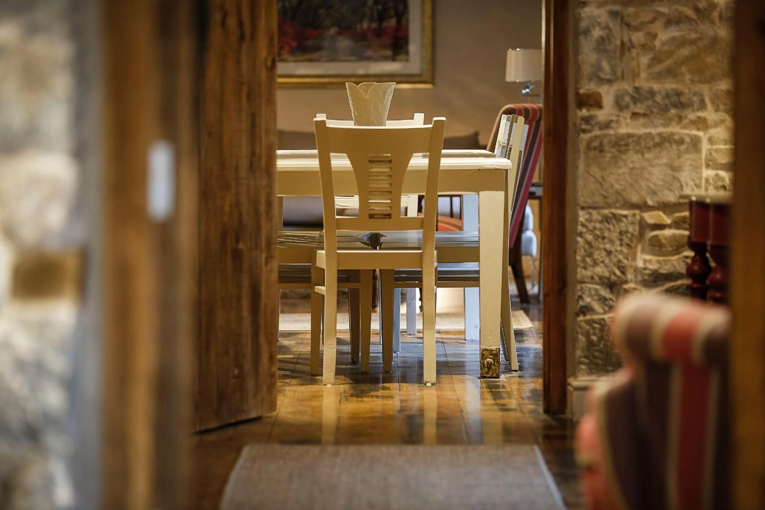 Una mesa de comedor de madera con sillas en una habitación con paredes de piedra y un cuadro colgado en la pared.