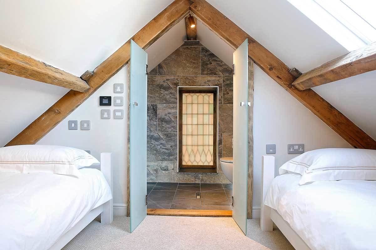 A bedroom with two beds, a stone fireplace, and a sloped ceiling.