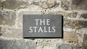 Un letrero que dice "THE STALLS" sujeto a una pared de piedra.