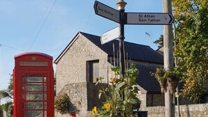 Una cabina telefónica roja tradicional, un edificio de piedra y un cartel con indicaciones a West Aberthaw y St Athan.
