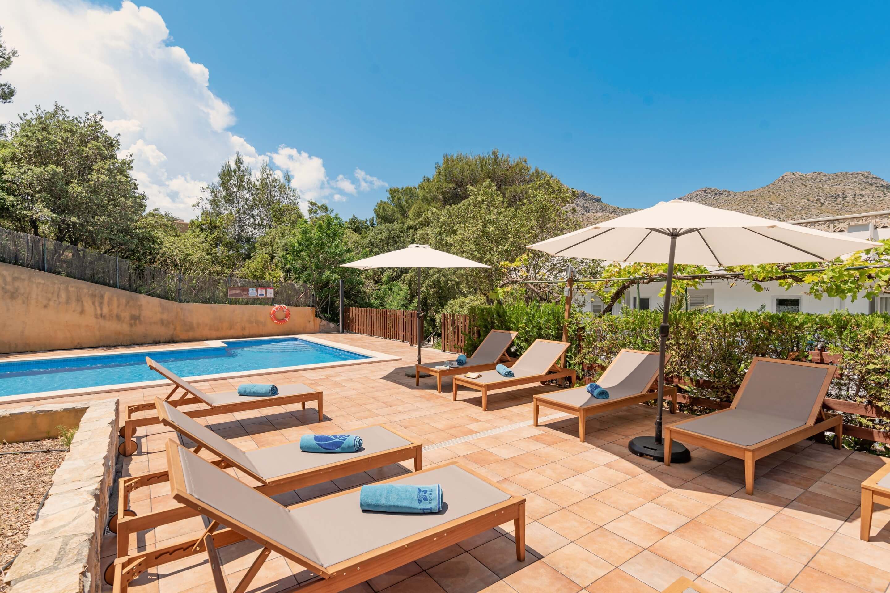 Un espace aménagé au bord de la piscine, avec des chaises longues et des parasols, entouré de verdure et offrant une vue sur les montagnes en arrière-plan.