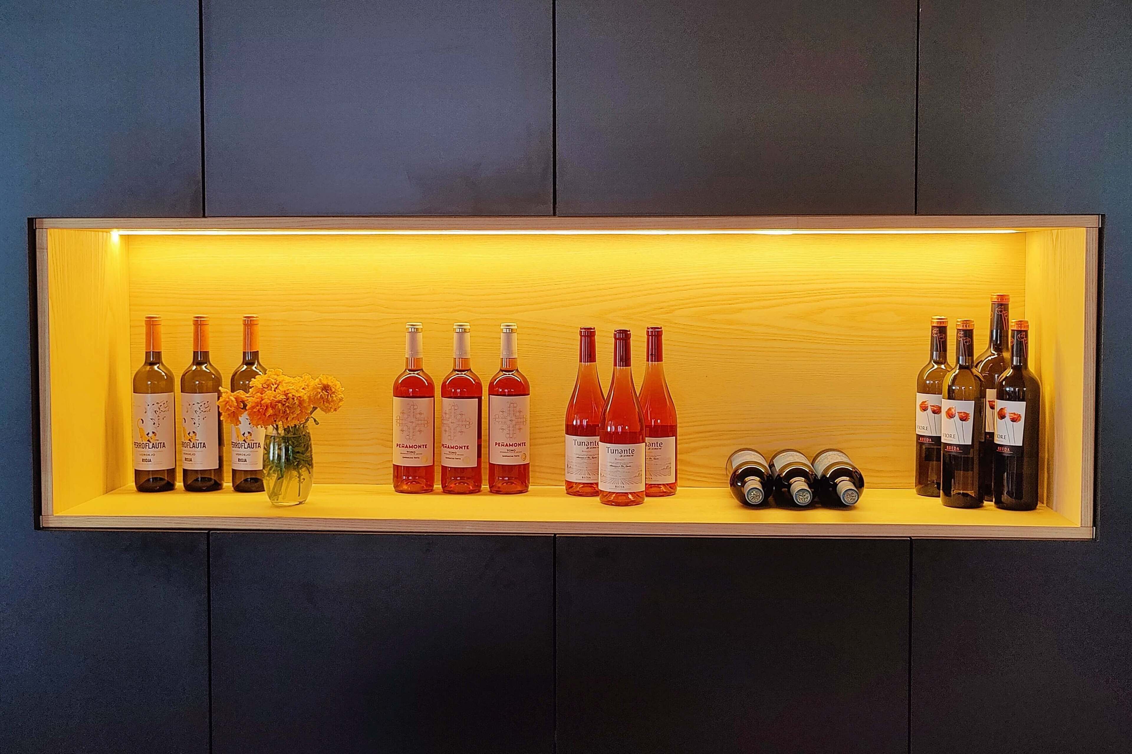 Una estantería para vinos con varias botellas y un florero.
