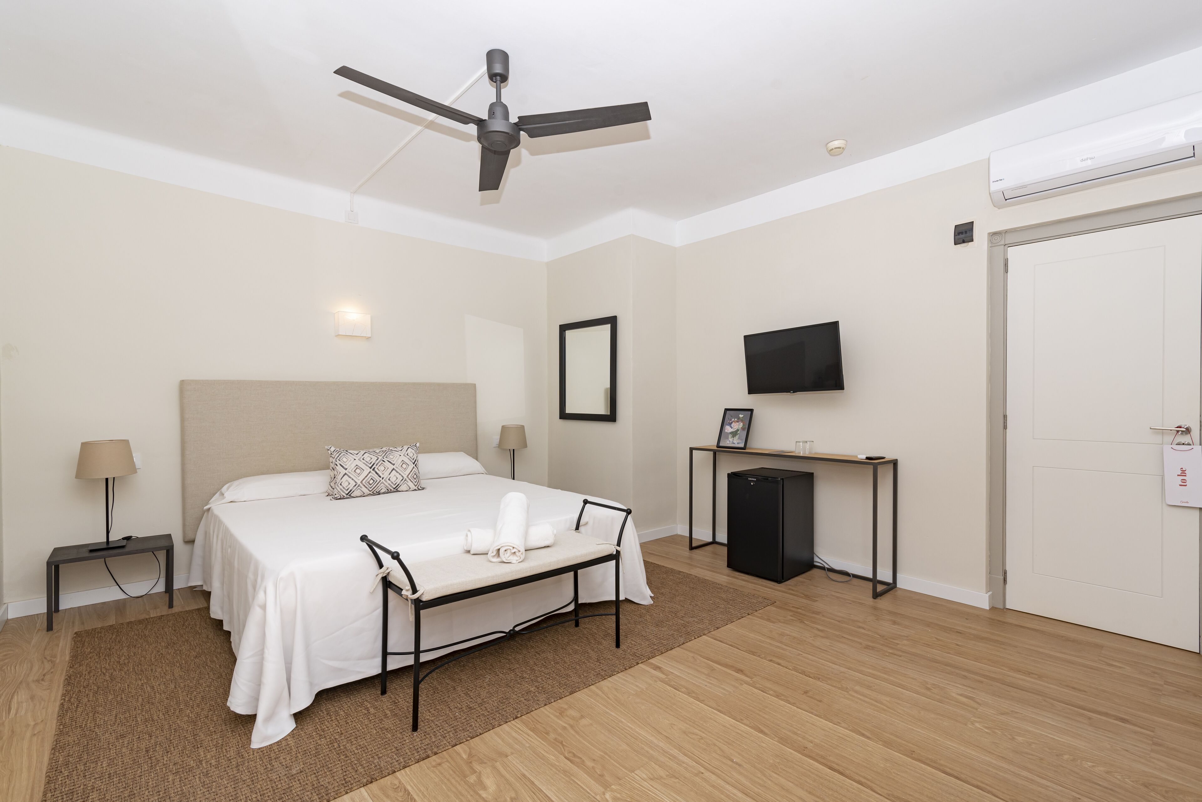 Ein Hotelzimmer mit Bett, Nachttischen, Schreibtisch, Fernseher und Deckenventilator.