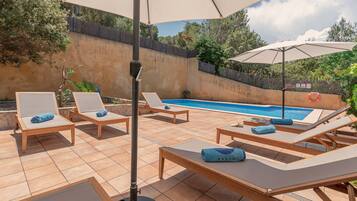 A poolside area with lounge chairs, umbrellas, and a swimming pool.