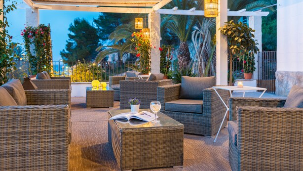 Une terrasse extérieure avec des meubles en osier, une table avec un livre et un verre, et des plantes en pot.