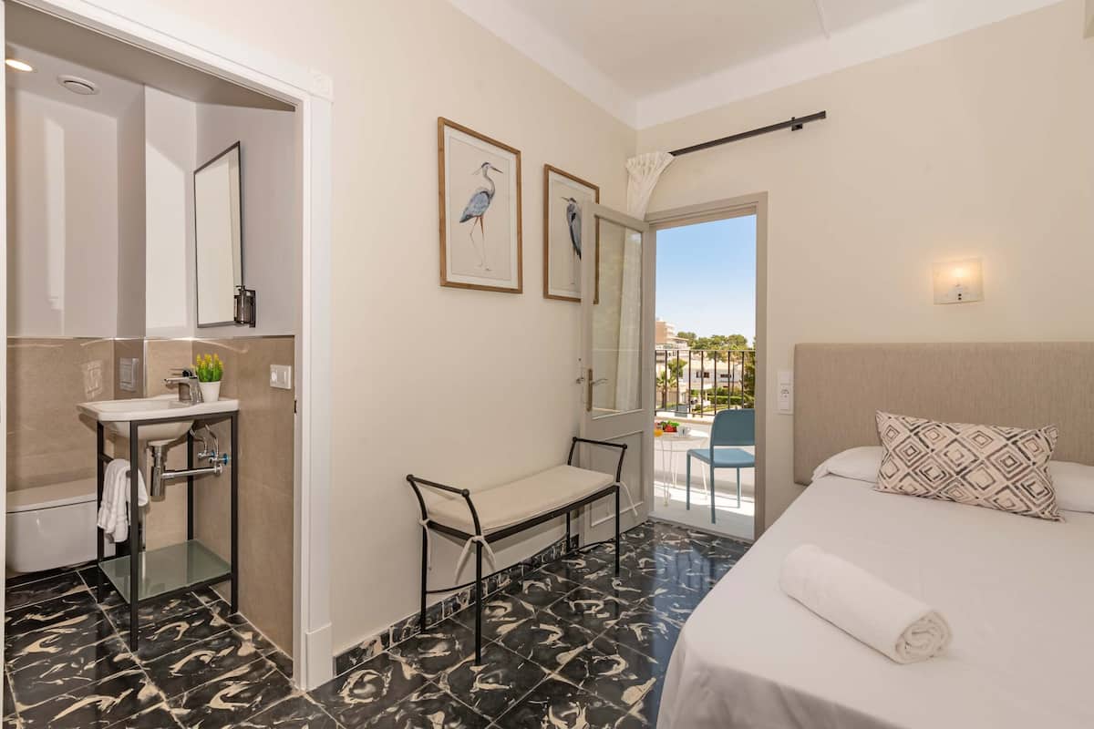 A hotel room with a bed, a bench, a sink, and a balcony with a view.