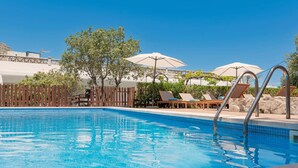 Une piscine entourée d’une clôture en bois et d’arbres, avec des chaises longues et des parasols.