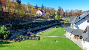 A house with a sloped roof, a garden with a pond, and a small dock.