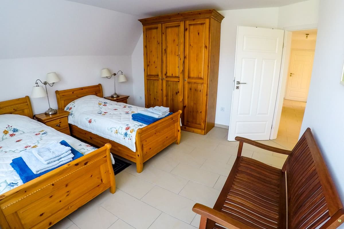 Quarto com duas camas de madeira, um guarda-roupa de madeira, uma porta branca e uma cadeira de madeira.