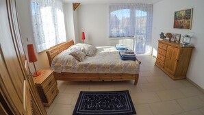 A bedroom with a wooden bed, a nightstand, a dresser, and a window with curtains.