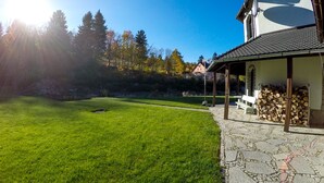 A well-maintained lawn, a stone pathway, and a building with a tiled roof and a stack of firewood.
