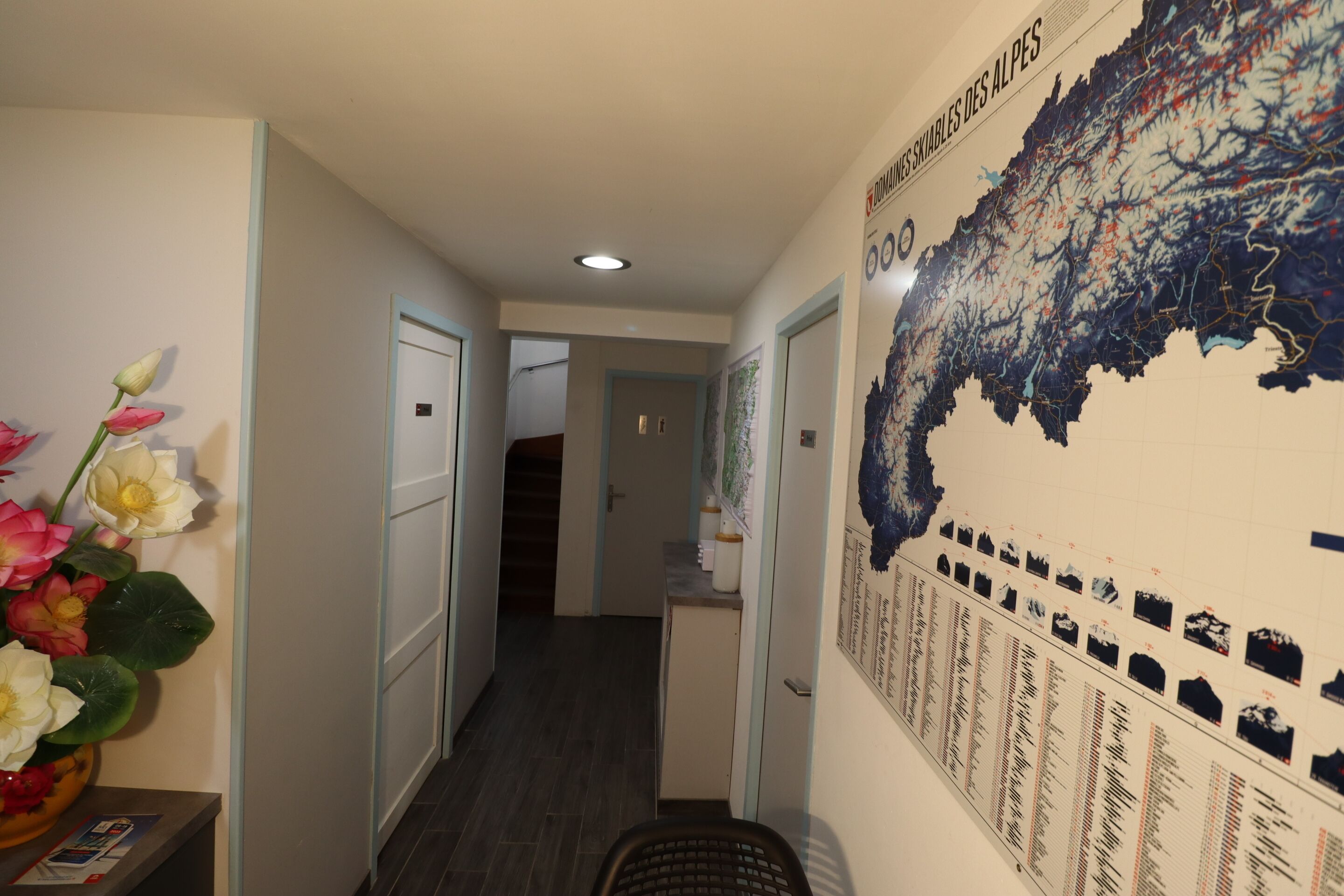 A hallway with a map on the wall, a staircase, and a flower arrangement.