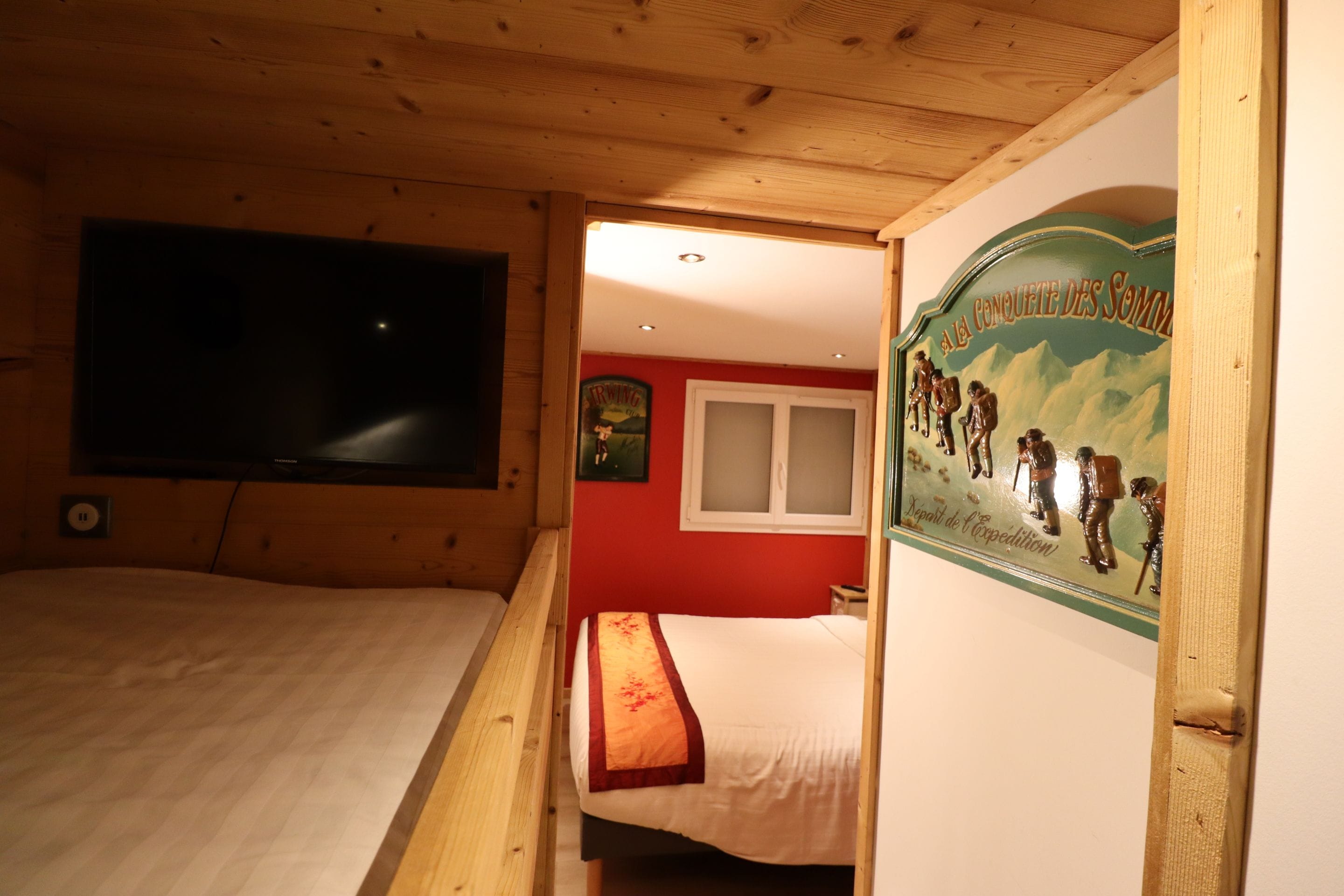 A room with two beds, wooden ceiling, a TV, and a wall with a mountain painting.