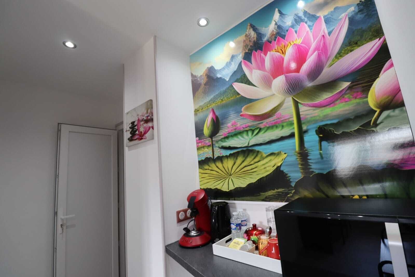 Une pièce décorée d’une grande fresque murale représentant une fleur de lotus, avec une machine à café rouge et un téléviseur noir posé sur un meuble noir.