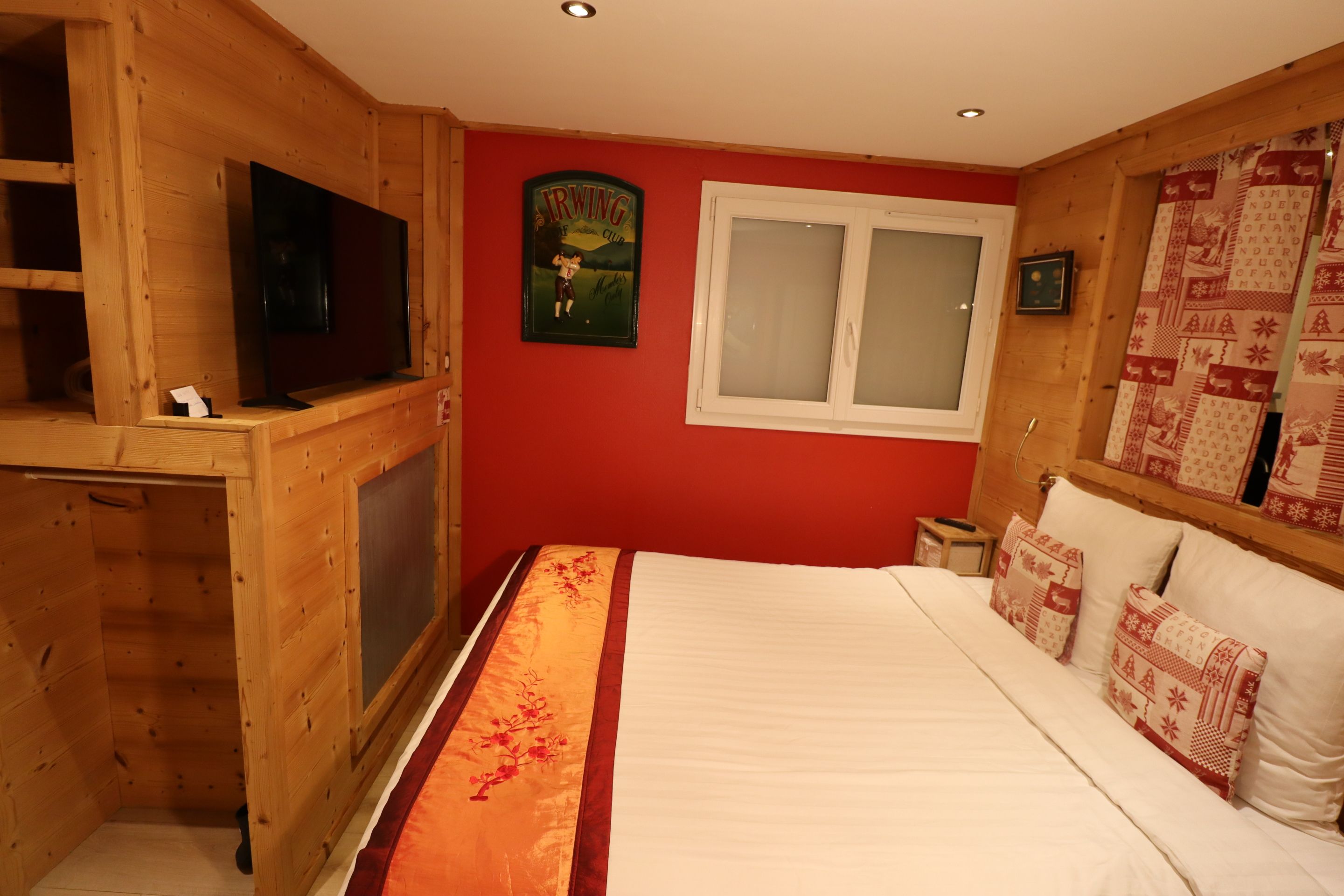 Habitación con paneles de madera, una cama, un televisor, una ventana y un tapiz acolchado.