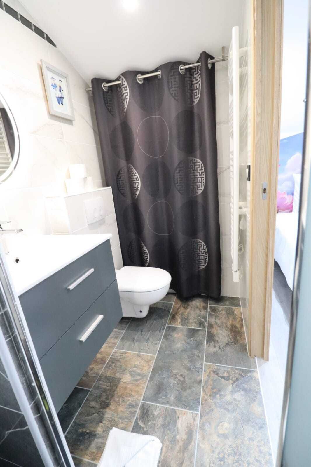 Een badkamer met toilet, wastafel met spiegel en douchegordijn met een geometrisch patroon.