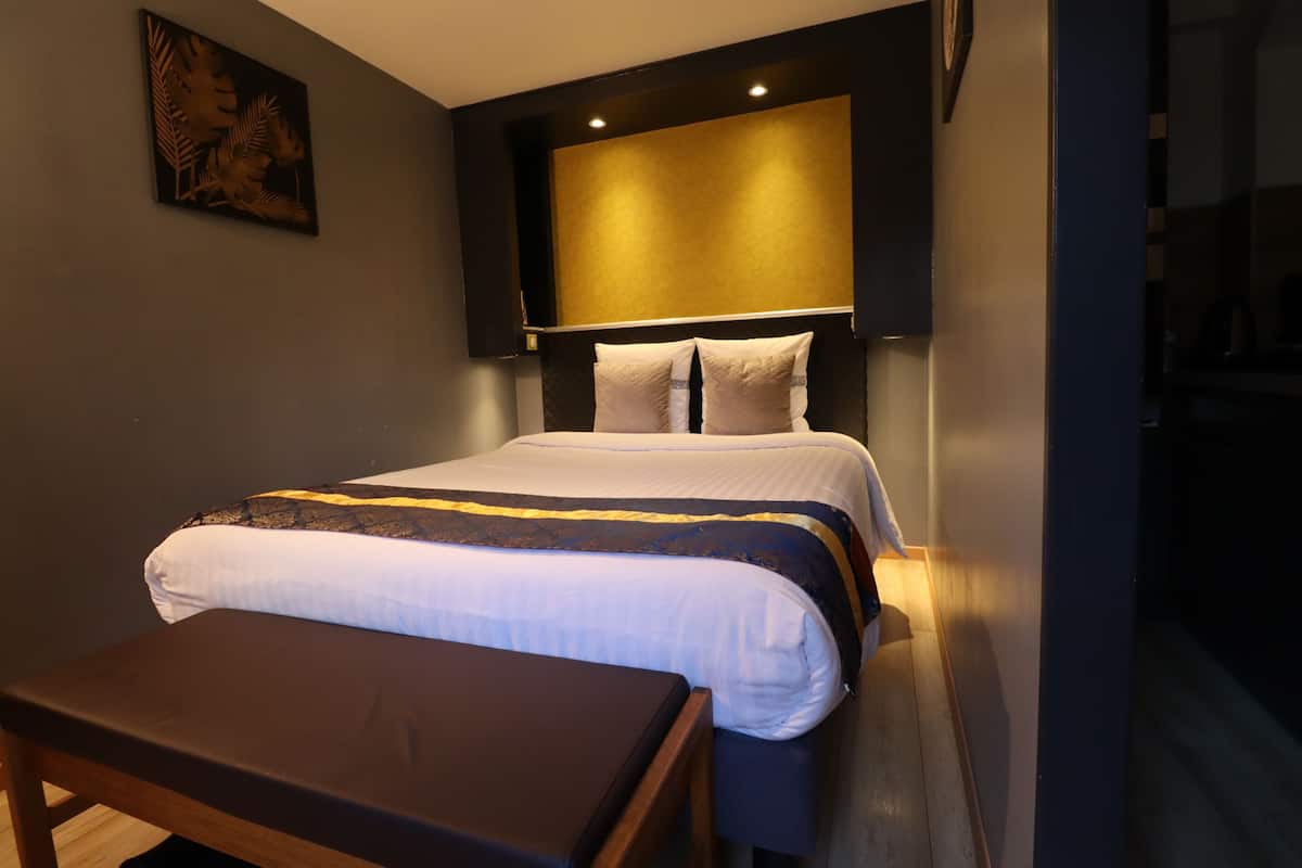 A modern hotel room with a neatly made bed, a bedside table, and a headboard with built-in lighting.