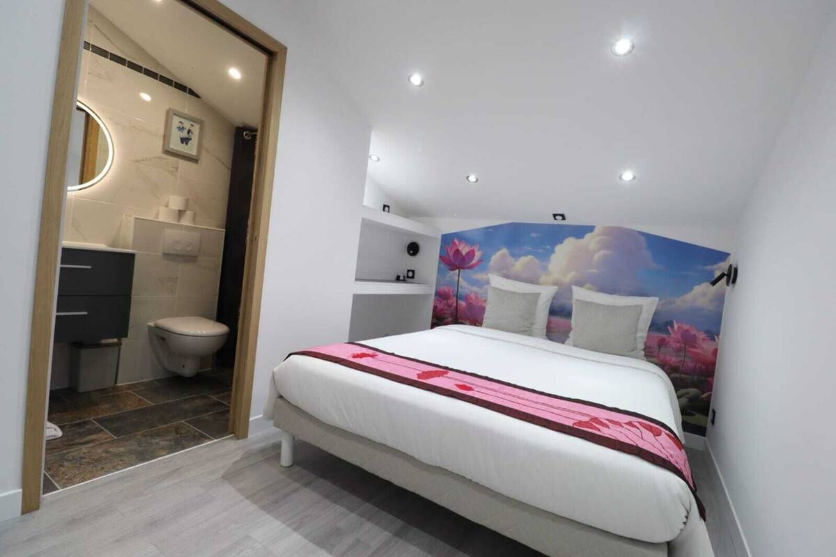 A bedroom with a bed, a bathroom with a toilet, and a wall with a floral mural.