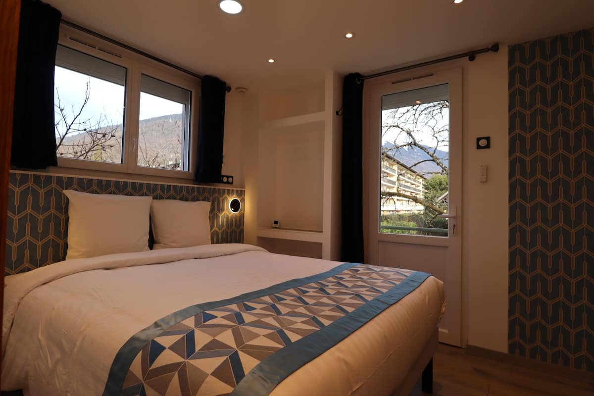 A bedroom with a large bed, a window with curtains, a door with a view, and patterned wallpaper.