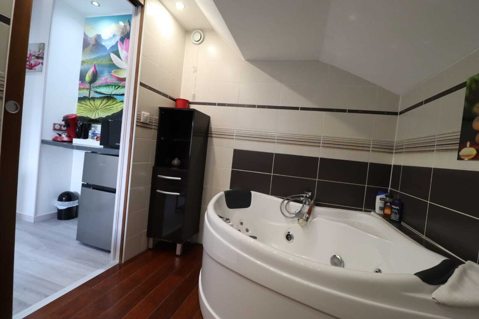 A bathroom with a large bathtub, a black cabinet with drawers, and a tiled shower area.