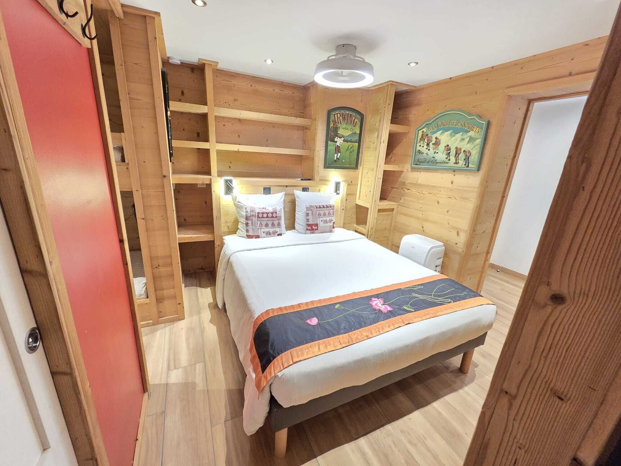 A wooden room with a bed, shelves, and a wall-mounted light fixture.