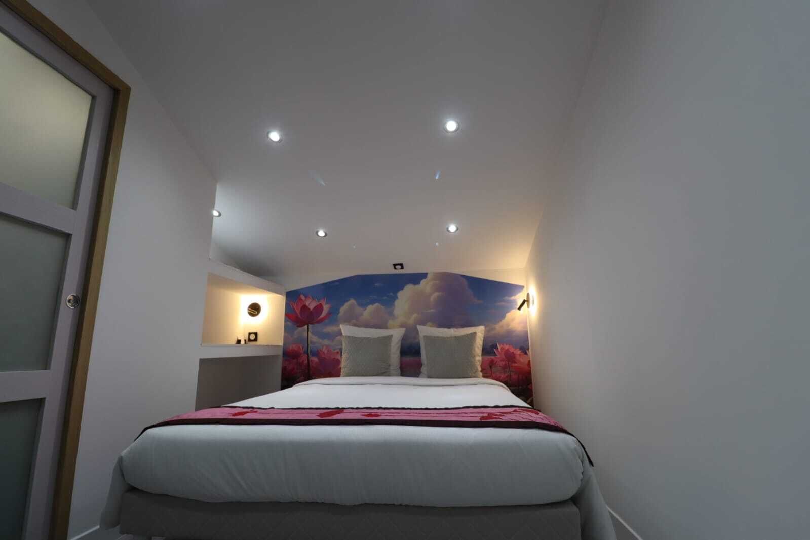 A bedroom with a bed, a nightstand, a wall-mounted lamp, and a ceiling light.