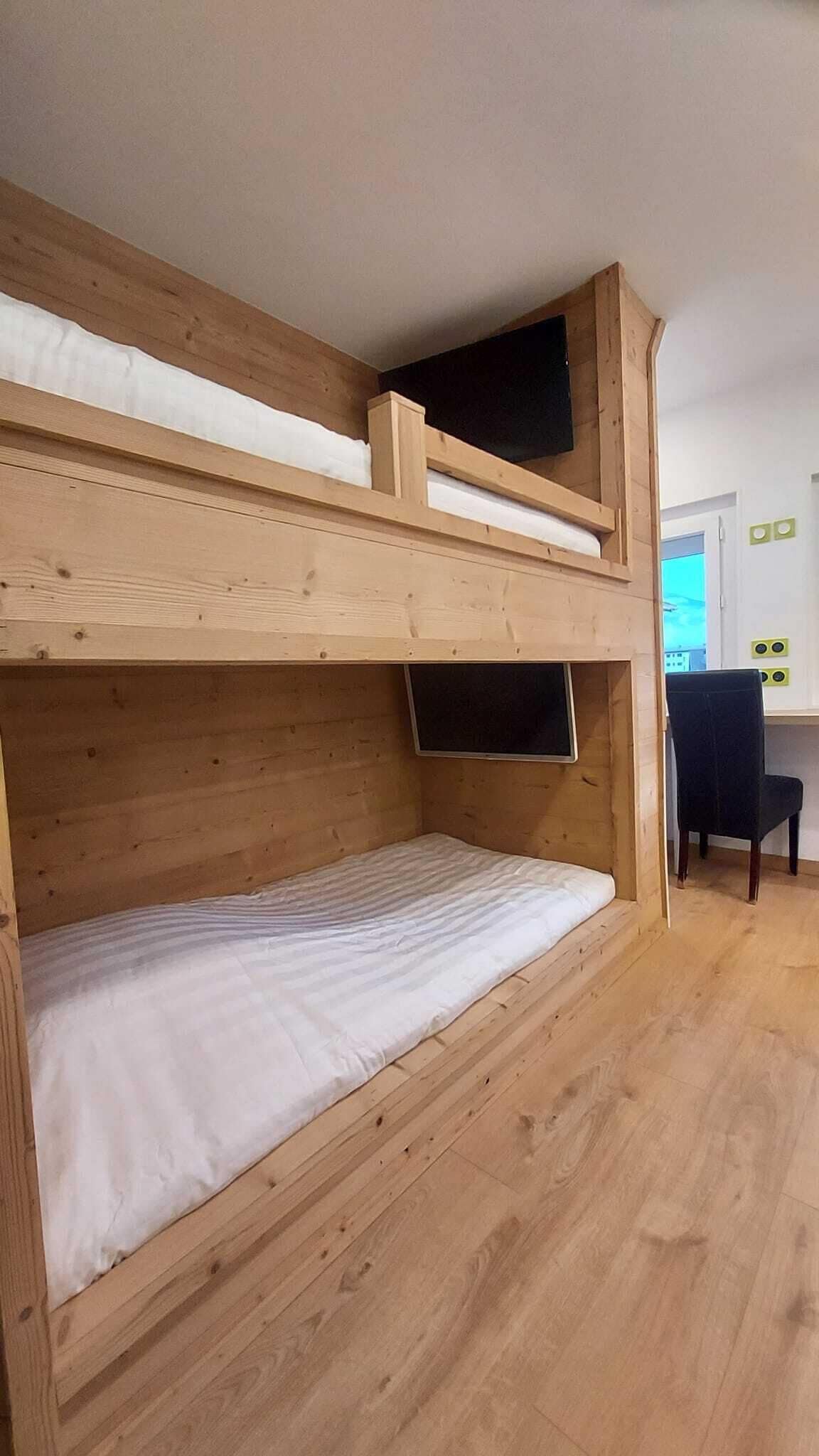Una cama litera con escritorio y silla en una habitación con suelo de madera.