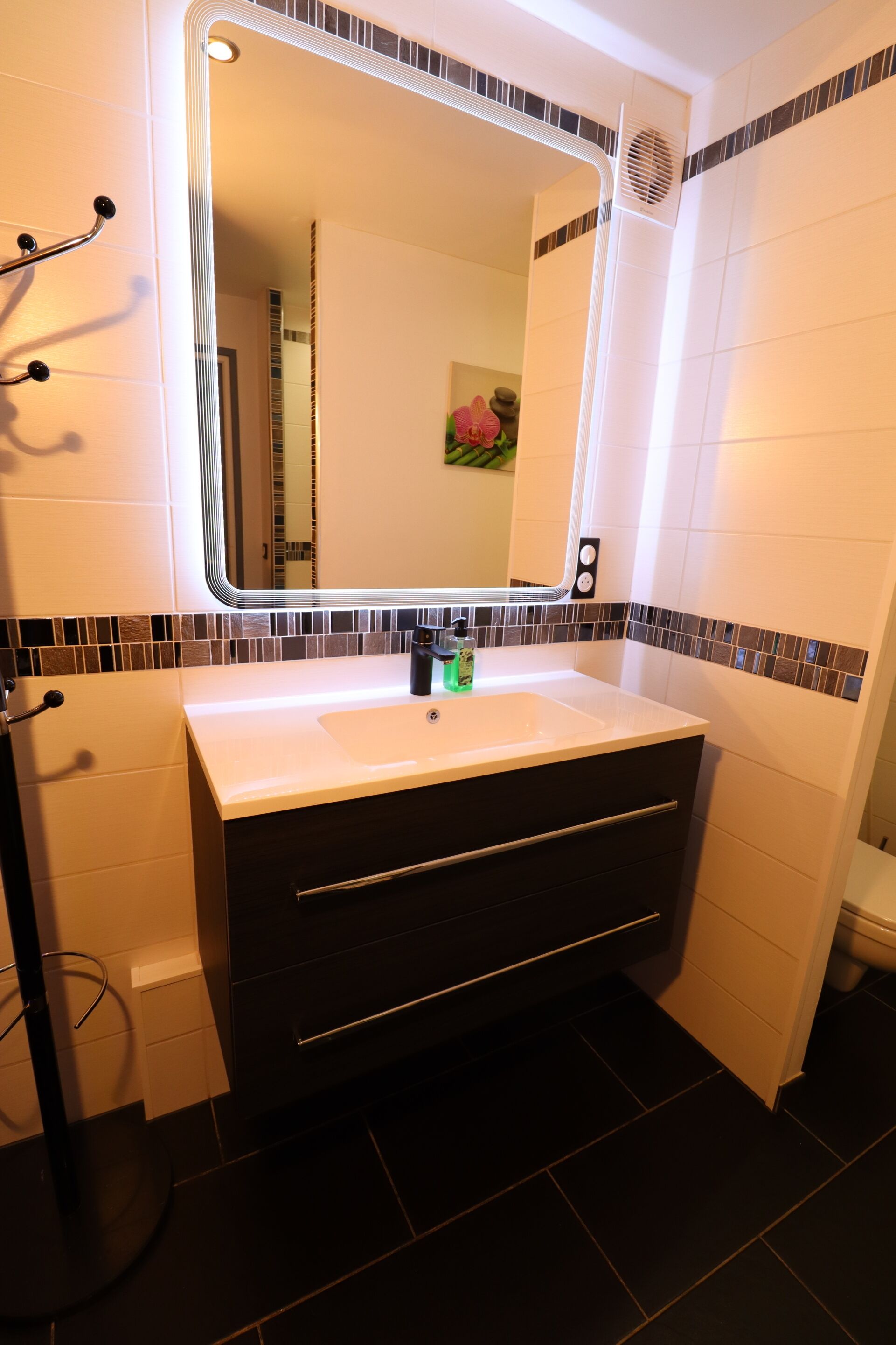 A modern bathroom with a white sink, dark cabinetry, and a mirror with a black frame.
