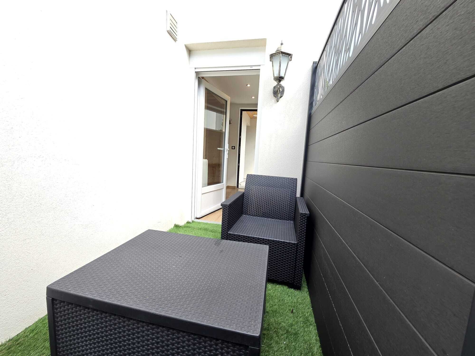 Un piccolo patio esterno con un tavolo e due sedie, una porta che dà su un ambiente interno e un punto luce fissato alla parete.