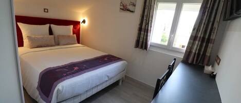 Un dormitorio con cama, una mesita de noche, una ventana con cortinas y un cuadro pequeño en la pared.