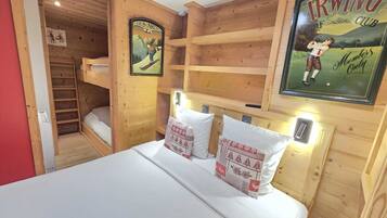 Une pièce en bois avec des lits superposés, un lit avec des oreillers, une affiche encadrée et une étagère.