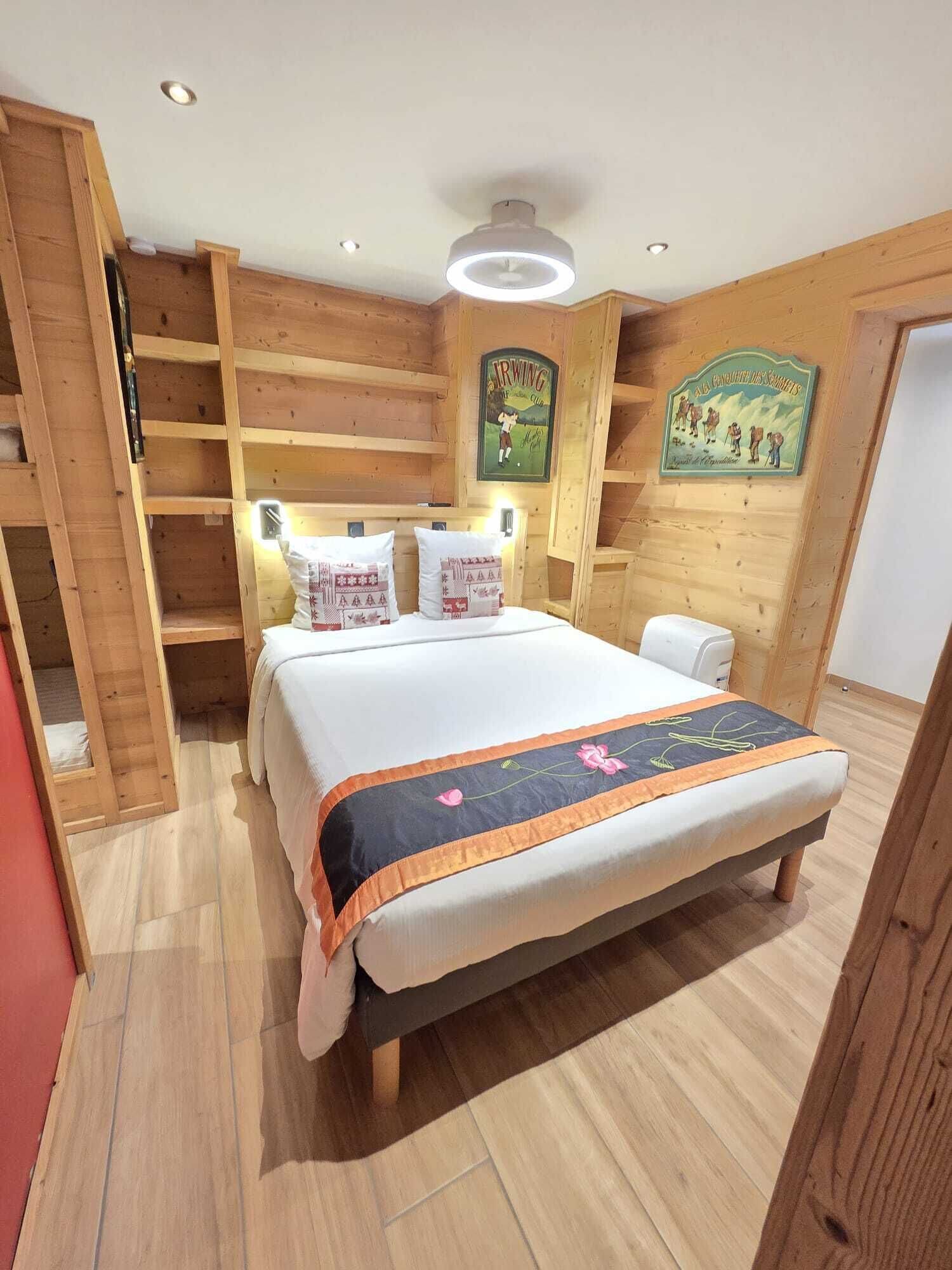 Una habitación de madera con una cama, un estante y un cuadro en la pared.
