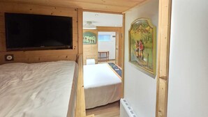 A wooden room with a bed, a TV, and a wall-mounted picture. - Le Lotus Blanc (Albertville)