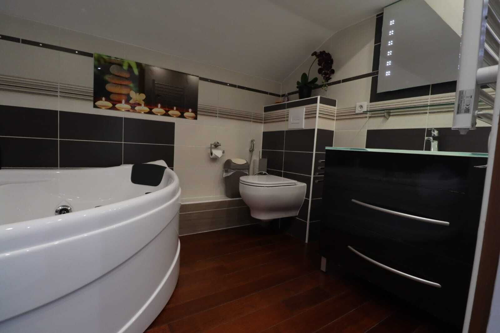 A modern bathroom with a large bathtub, a toilet, and a black vanity with a mirror.