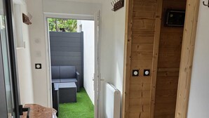 A hallway with a wooden door, a radiator, and a view of a patio with outdoor furniture. - Le Lotus Blanc (Albertville)
