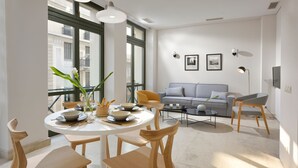 Un espace repas moderne avec une table ronde, des chaises en bois et une vue sur le paysage urbain grâce à de grandes fenêtres.