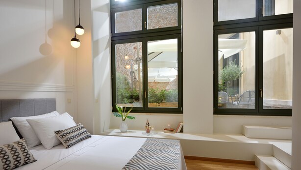 Une chambre moderne avec un grand lit, une fenêtre donnant sur l’extérieur et un banc intégré le long de la fenêtre.