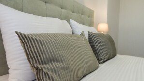 A bed with a tufted headboard, white and striped pillows, and a bedside lamp. - Rs porto Apartments (Porto)