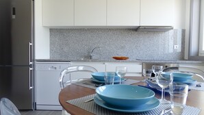 A modern kitchen with white cabinets, granite countertops, and a dining area with blue plates and clear glassware. - Rs porto Apartments (Porto)