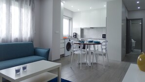 A modern living room with a sofa, a dining table, and a kitchen area in the background. - Rs porto Apartments (Porto)