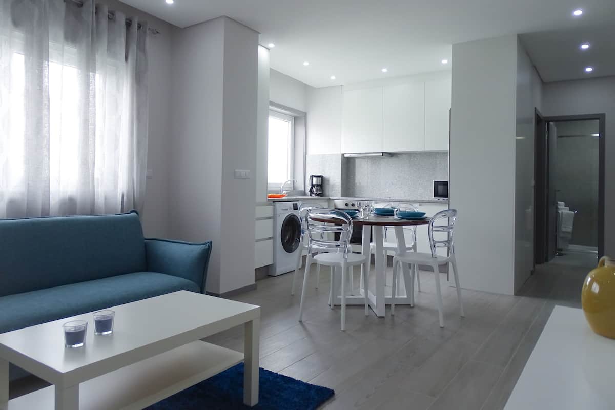 A modern living room with a sofa, a dining table, and a kitchen area in the background.