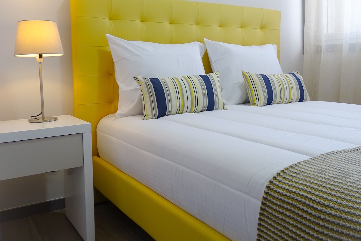 A bed with a yellow headboard, white bedding, and striped pillows.