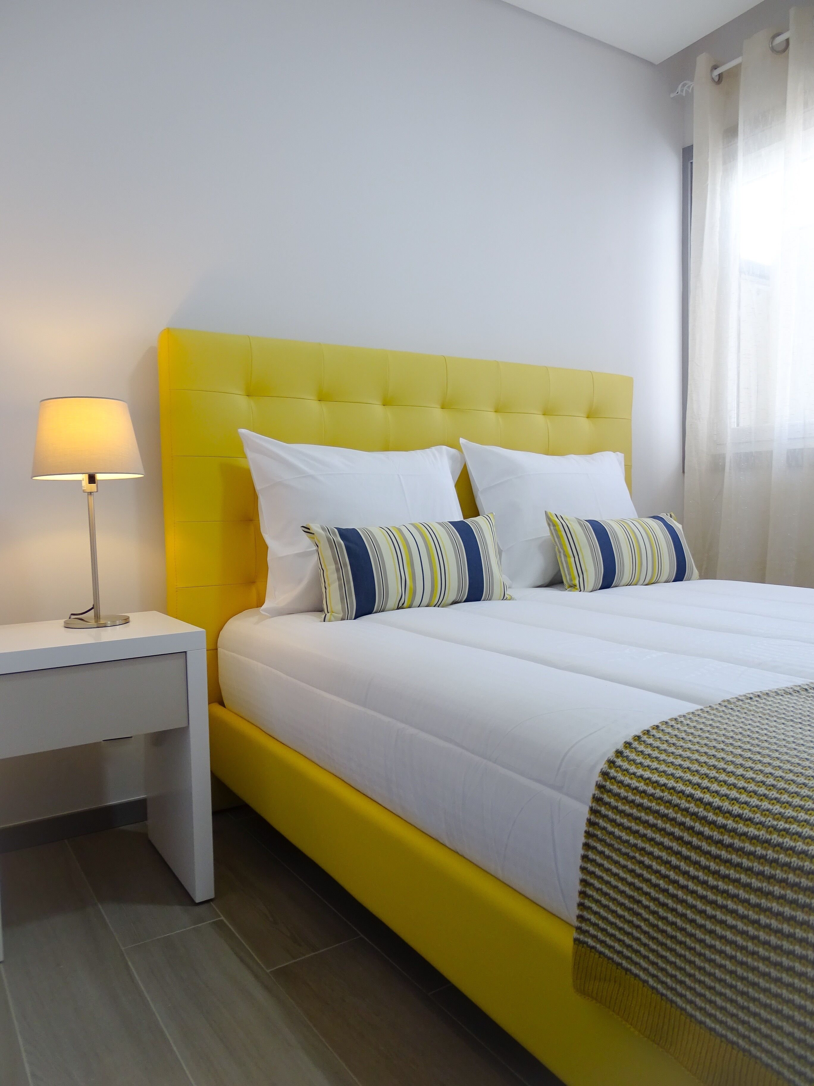 A bed with a yellow headboard, white bedding, and striped pillows.